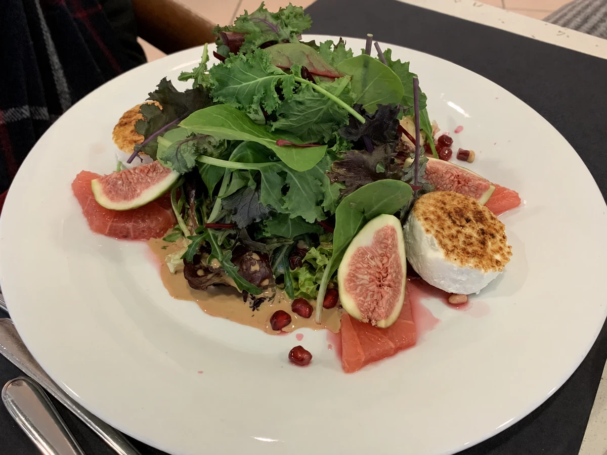Leafy salad with figs, citrus, pomegranate seeds and cheese on a white plate.